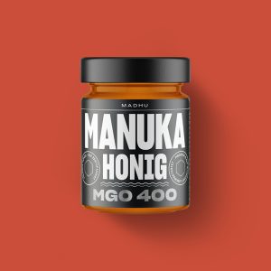 Abgebildet ist ein Manuka-Honige MGO30 und MGO205, jeweils in einem 250Gramm Glas. Zusätzlich auf dem Bild 2 schwarze Dosen mit Manuka Bonbons und ein Heft mit Manuka-Honig Rezepten.